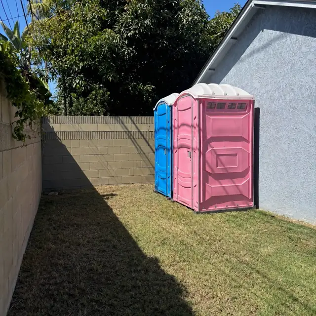 Two porta potties beside a backyard wall